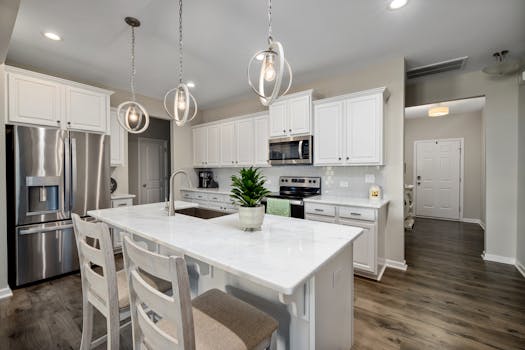 A spacious and modern kitchen with white cabinets and elegant hanging lights.