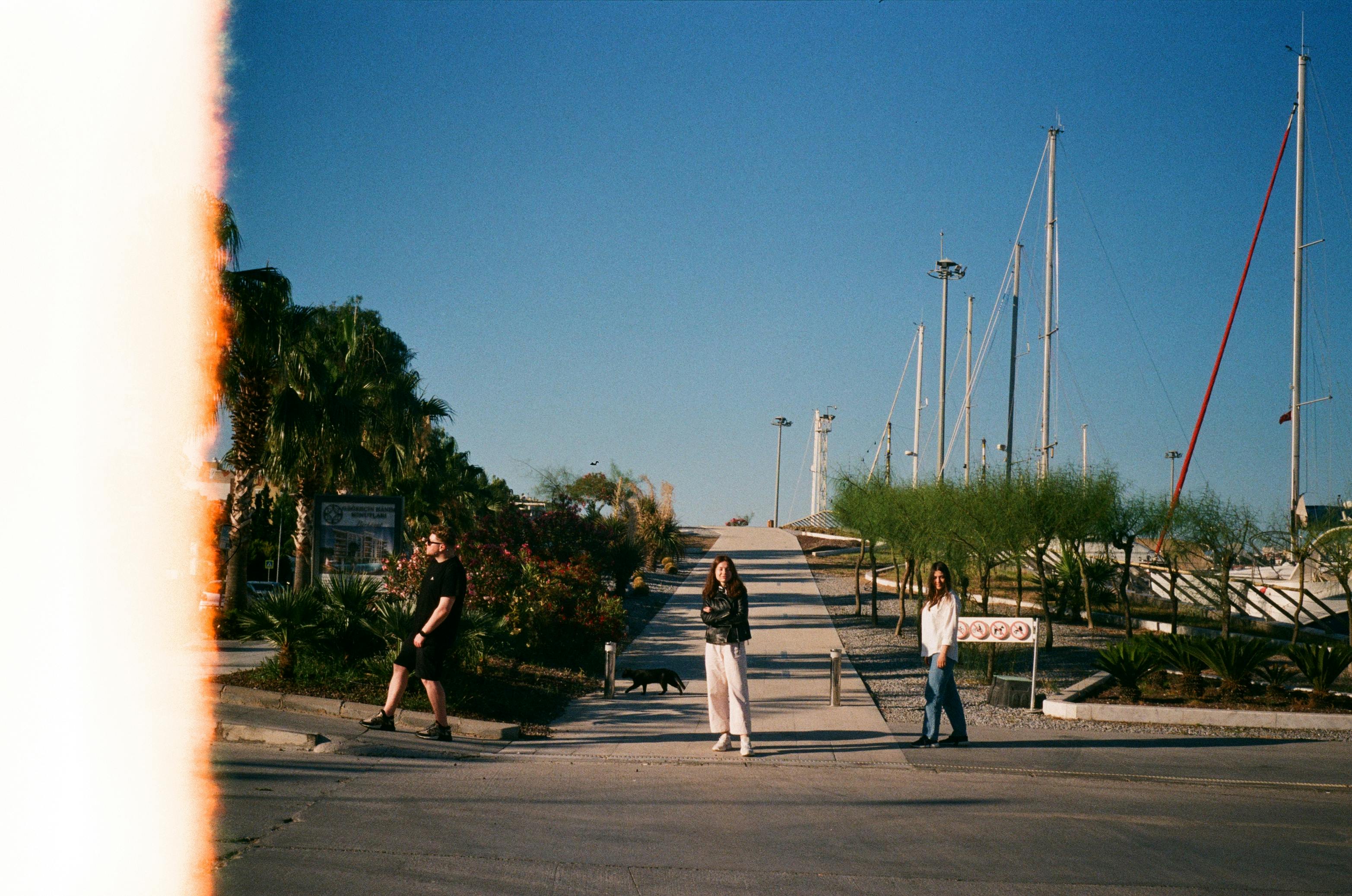 Three people at a marina under a clear blue sky on a sunny day.