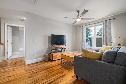 Bright modern living room featuring wooden flooring, a grey sofa, and a ceiling fan.