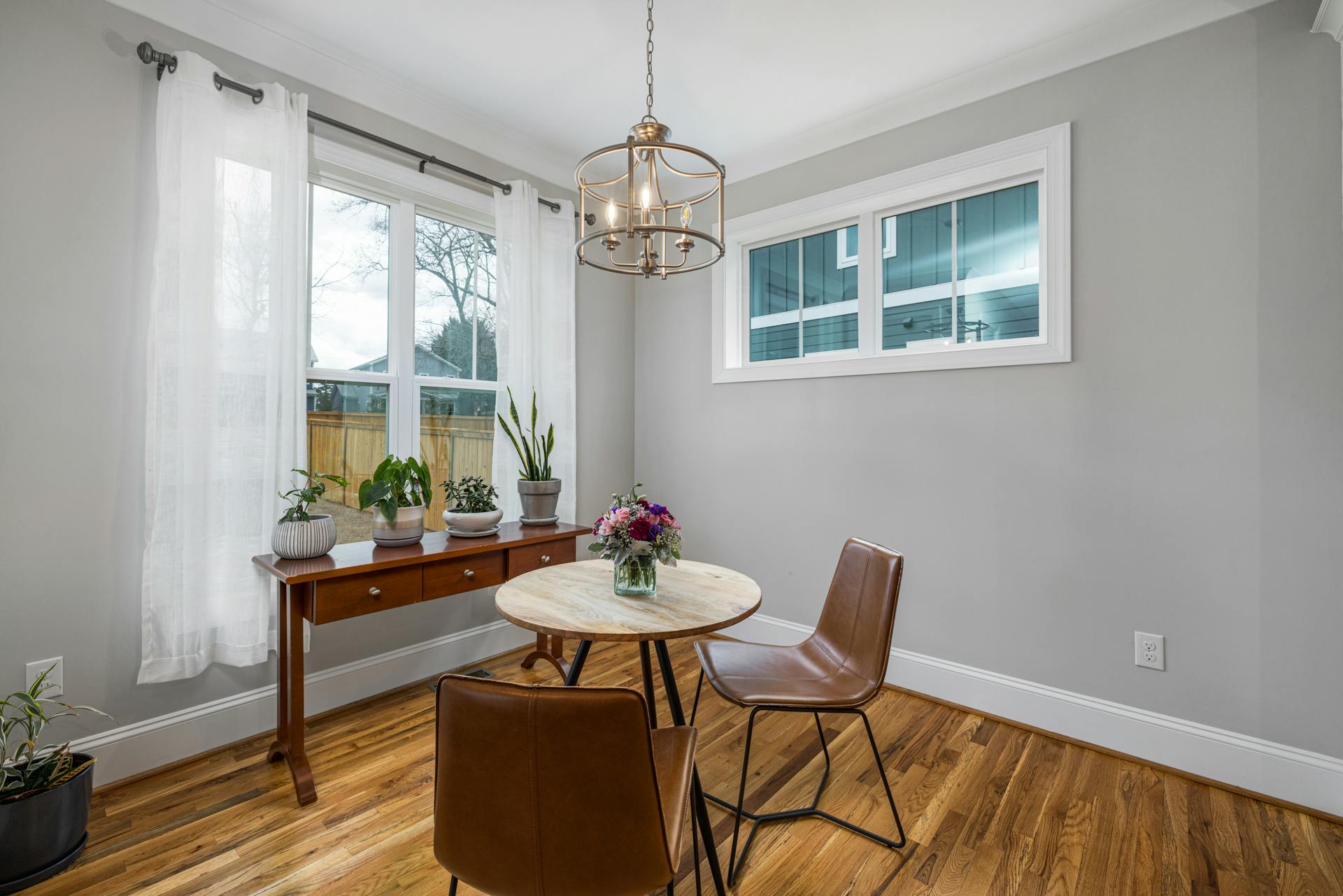 A stylish dining nook featuring a wooden table, chairs, and vibrant plants, bathed in natural light.