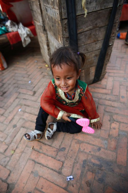 Free A young girl with a toy sits outdoors, smiling and enjoying her playtime. Stock Photo