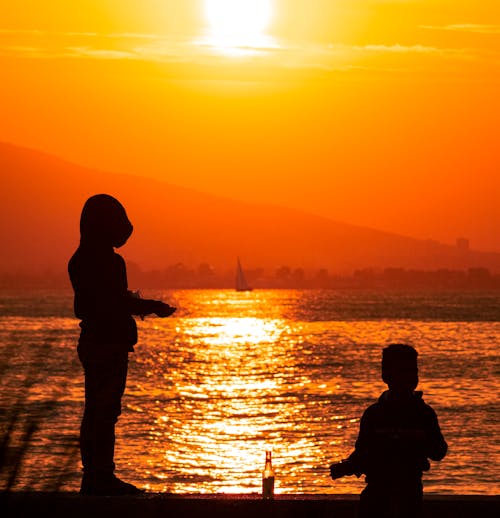Free Silhouette of Two People by the Riverside during Golden Hour  Stock Photo