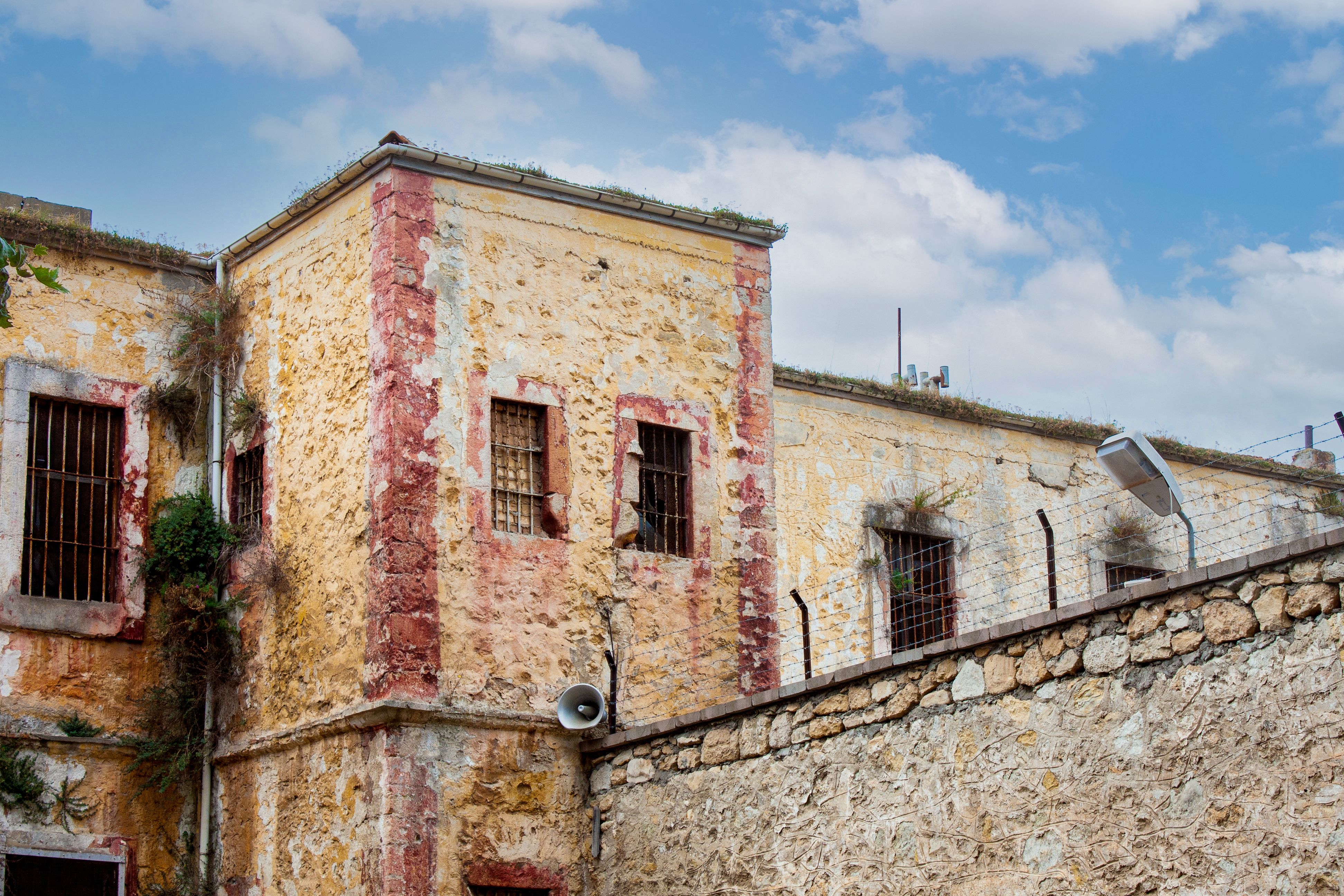 Old stone prison building with barred windows and rusty walls under a blue sky.