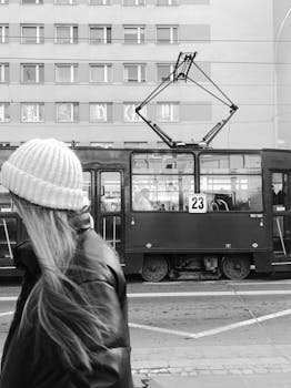 A monochrome view of a tram and woman in a Polish city, capturing urban public transport vibes.
