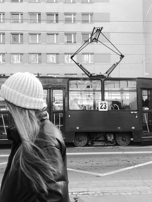 A monochrome view of a tram and woman in a Polish city, capturing urban public transport vibes.