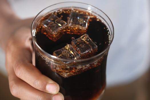 Close-up of a hand holding a glass of dark soda with ice cubes, creating a refreshing feel.
