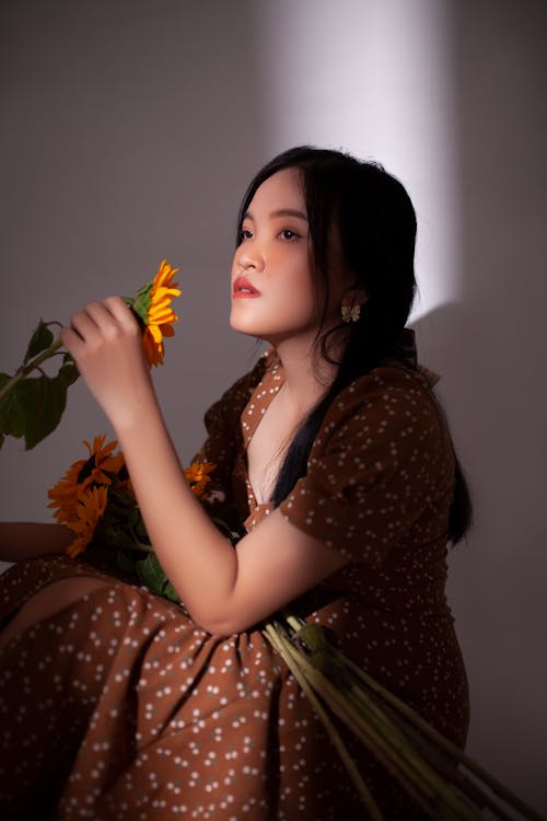 Woman in Dress Sitting and Holding Sunflowers