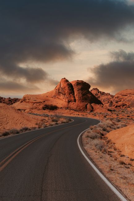 Scenic winding road in desert with red rock formations and dramatic clouds, NV, USA.