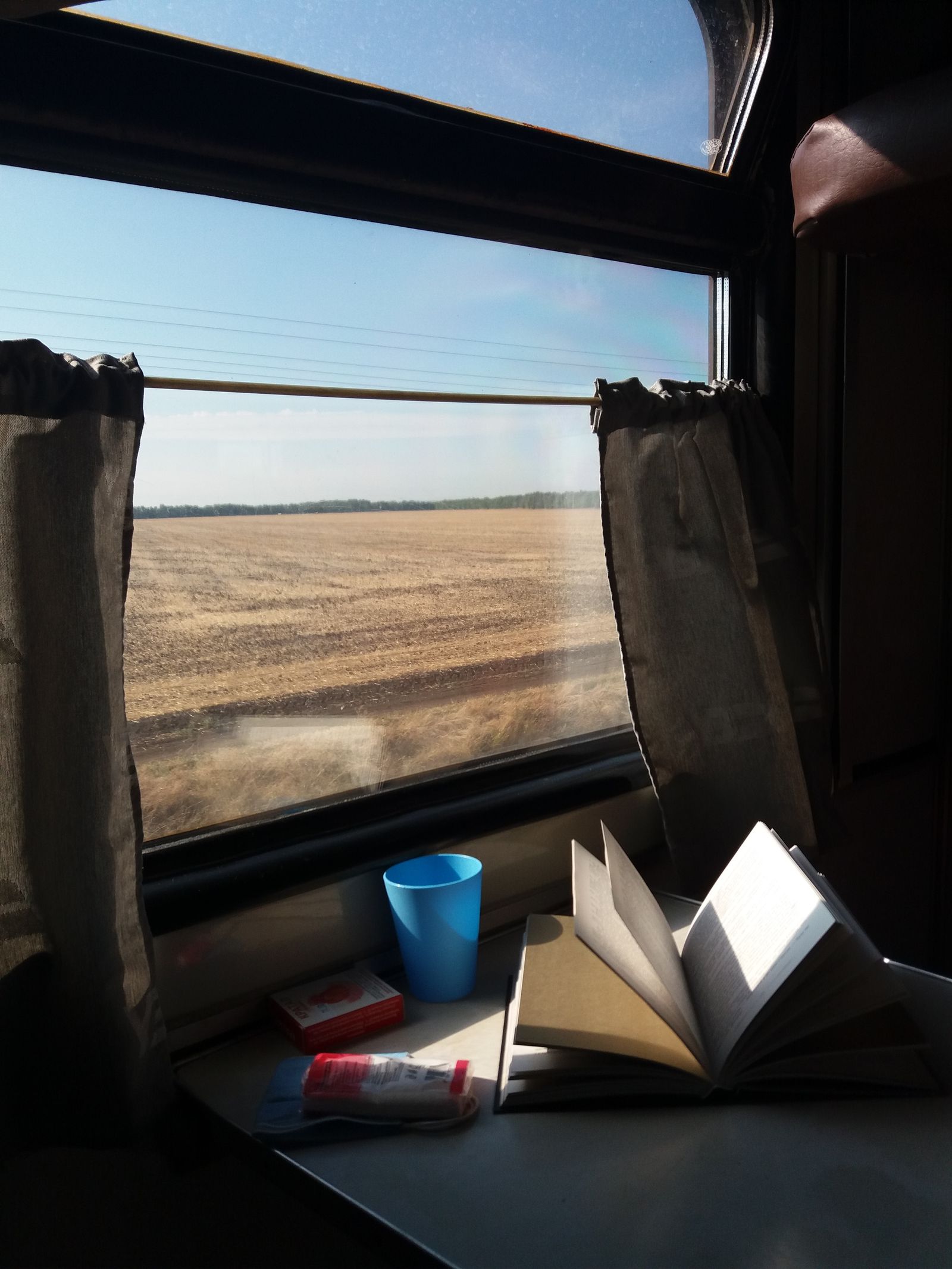 Train window over open fields with a book on the table