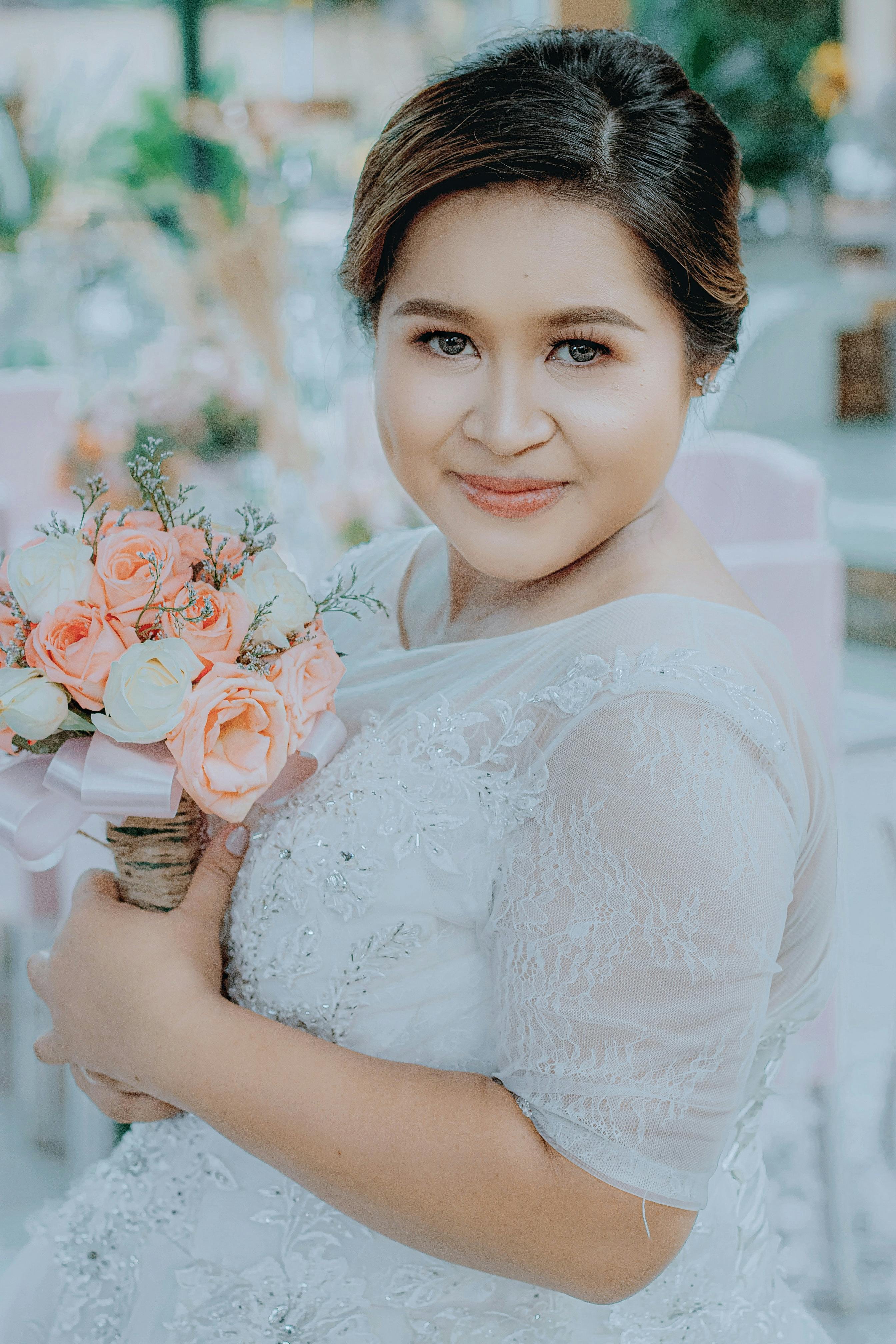 Beautiful Asian bride in an elegant white wedding dress holding a bouquet and smiling warmly.