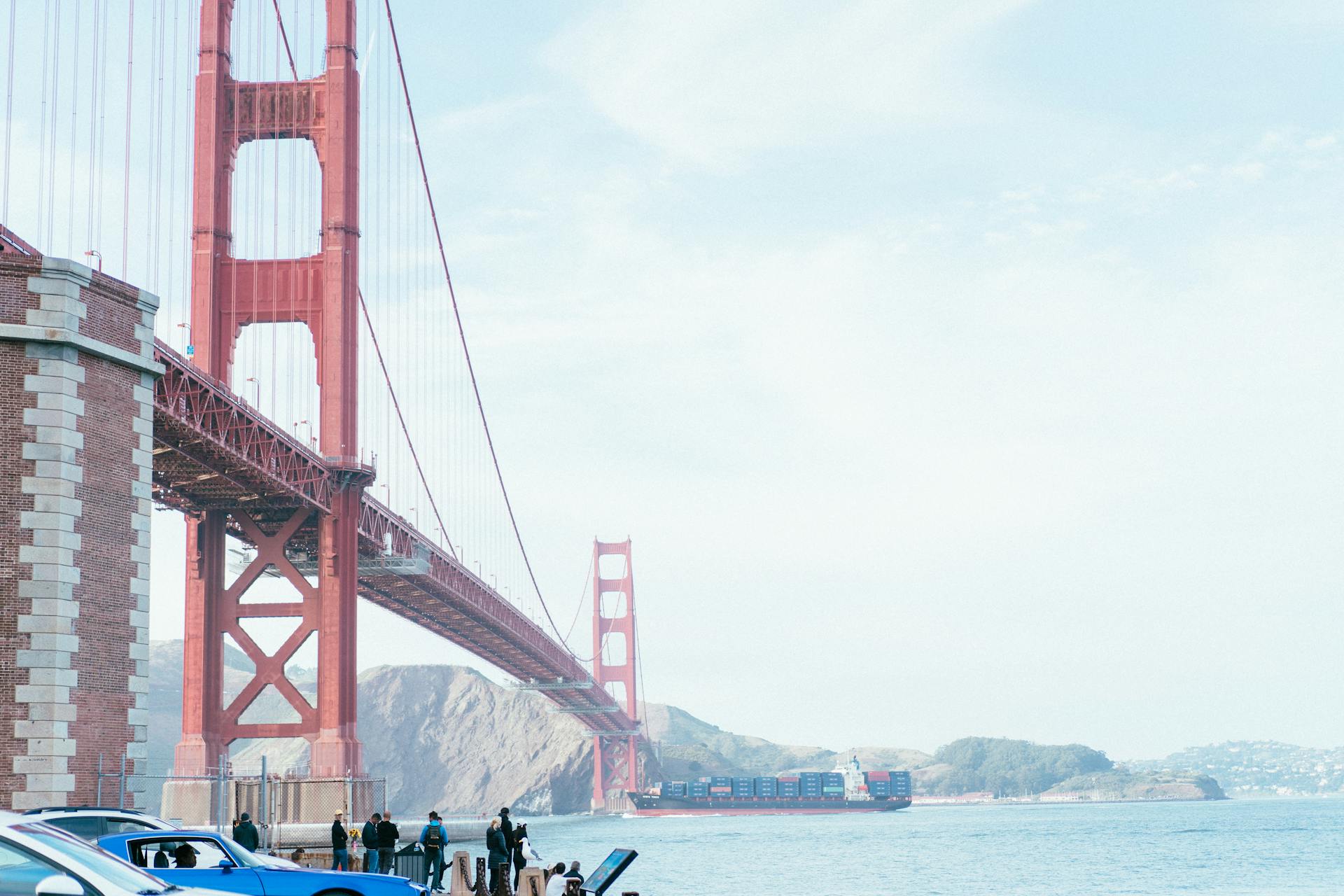 A view of the iconic Golden Gate Bridge with a container ship passing beneath on a sunny day.