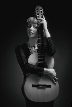 Elegant black and white portrait of a woman holding a classical guitar, exuding sophistication.