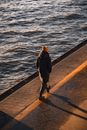 Man in Black Jacket and Black Pants Walking on Concrete Dock
