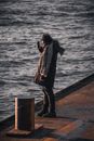 Man in Black Jacket and Black Pants Standing on Brown Wooden Post Near Body of Water