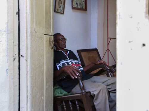 Free A senior man sits peacefully in an armchair, captured through a doorway in a cozy indoor setting. Stock Photo