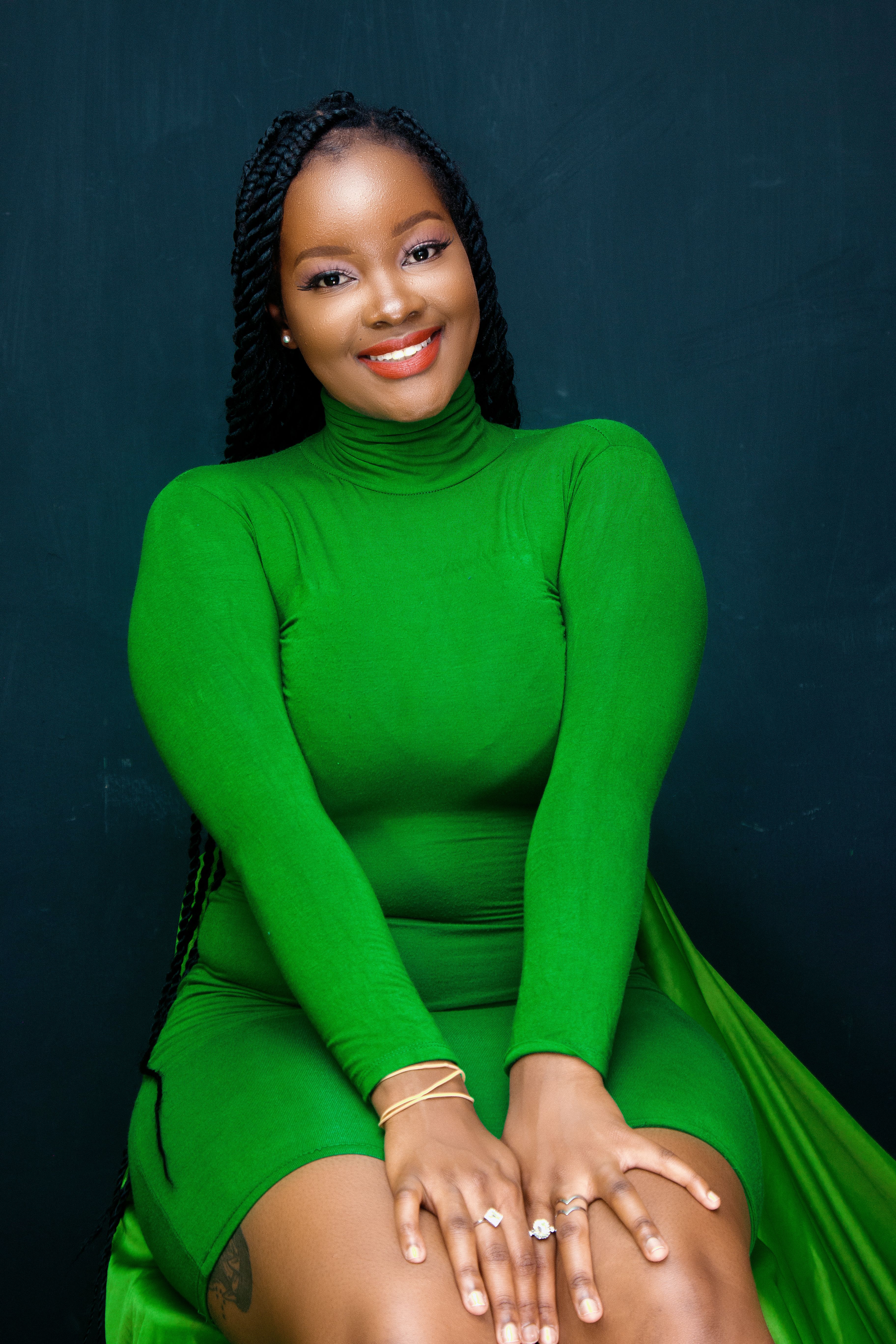 Studio portrait of a smiling woman in a vibrant green dress with braided hair.