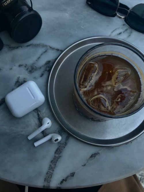 Free Chic composition featuring iced coffee, wireless earbuds, and sunglasses on a marble table. Stock Photo