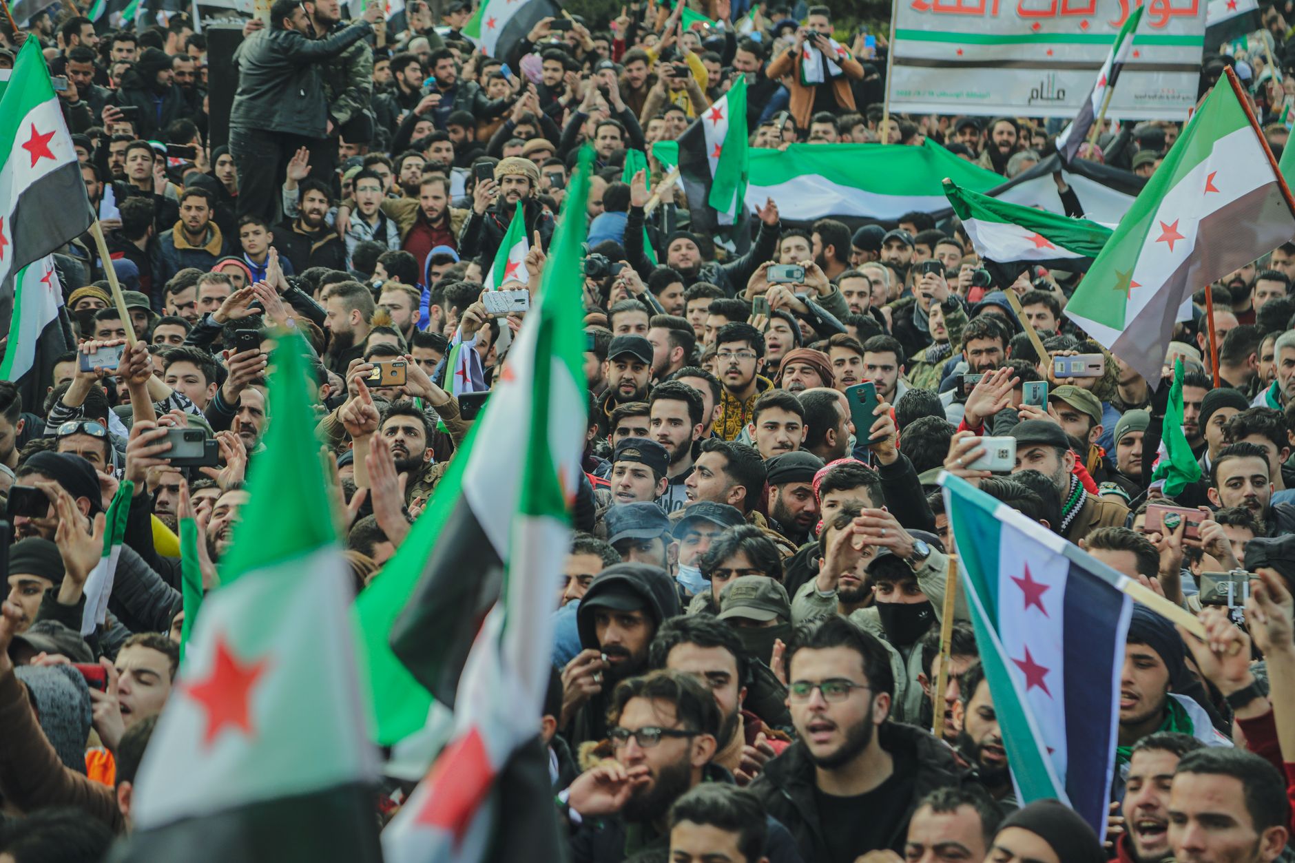 Large crowd in Syria waving flags during a protest, demonstrating unity and political expression.