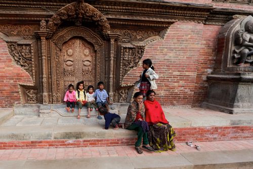 Free A group of children sitting by a decorated temple entrance, featuring intricate woodwork. Stock Photo