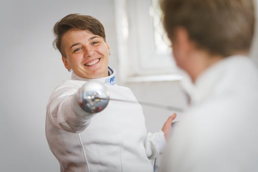 A close-up of a smiling female fencer practicing indoors with a foil.