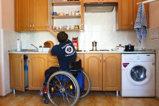 An individual in a wheelchair reaching for a kitchen shelf, demonstrating accessibility.