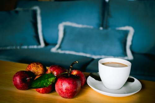 White Ceramic Cup on White Ceramic Saucer Beside Red Apple Fruits