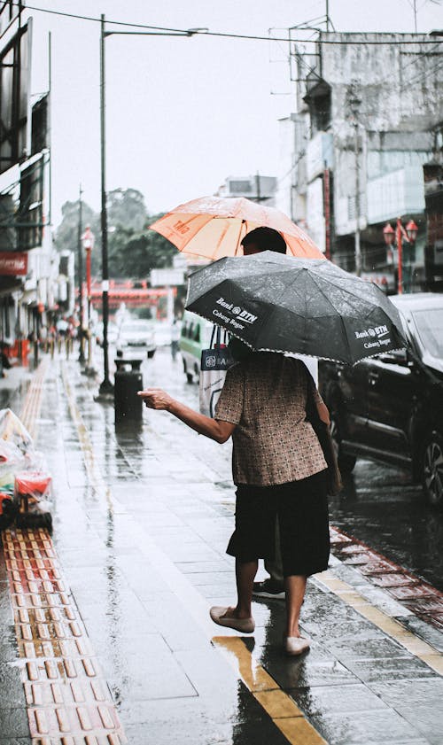Free Woman in Brown and Black Polka Dot Shirt Holding Umbrella Walking on Sidewalk Stock Photo