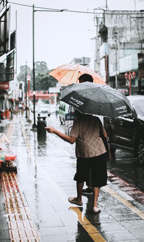 Free A person with umbrellas walking on a rainy street in West Java, Indonesia, capturing a gloomy street photography vibe. Stock Photo