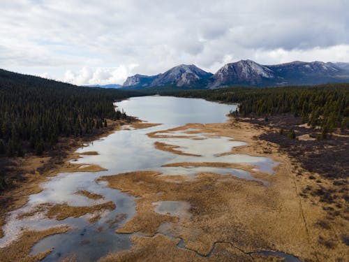 Scenic View of Land and Rocky Mountains under Cloudy Sky 