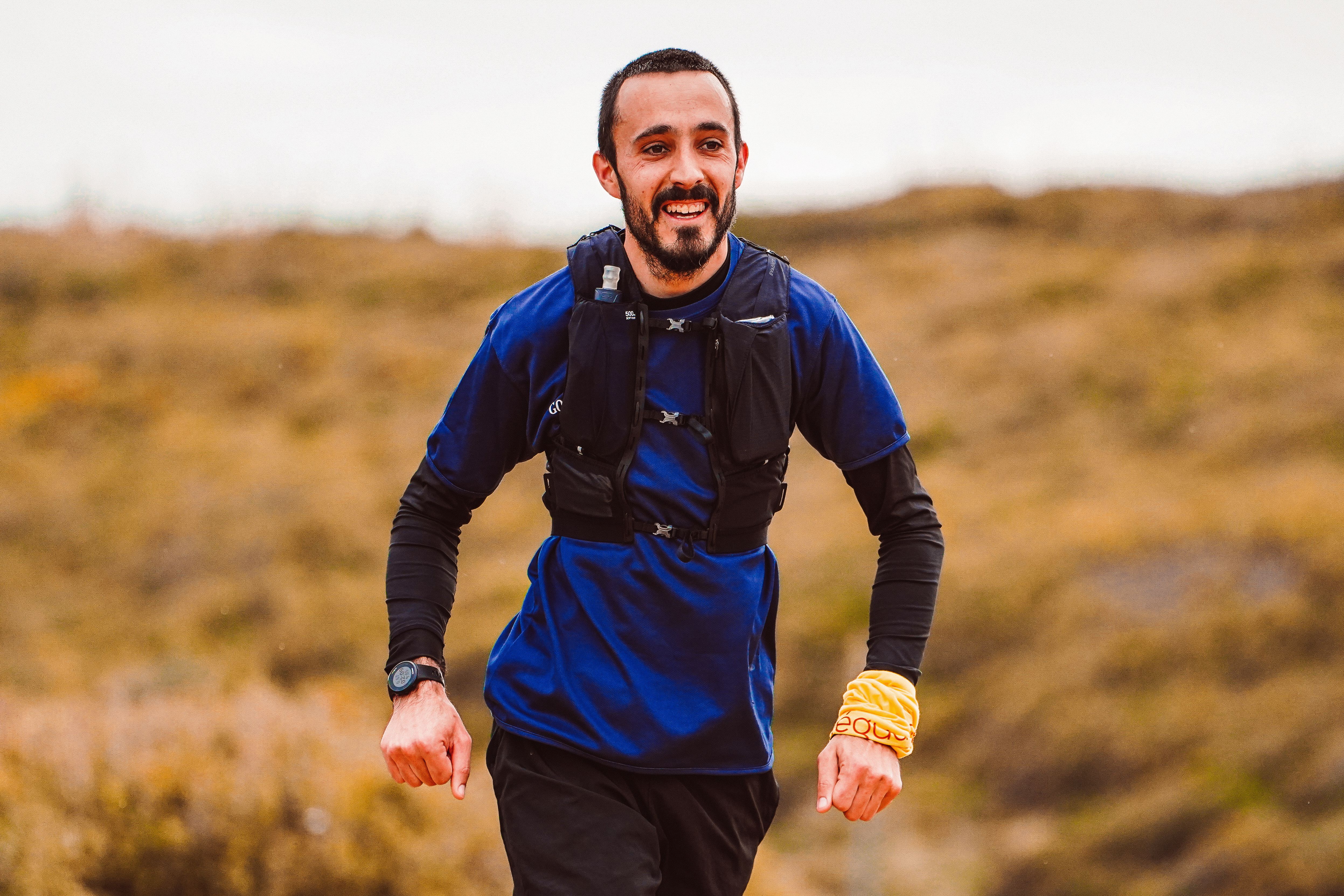 Runner smiling while jogging on a scenic trail, heart rate monitor visible on wrist