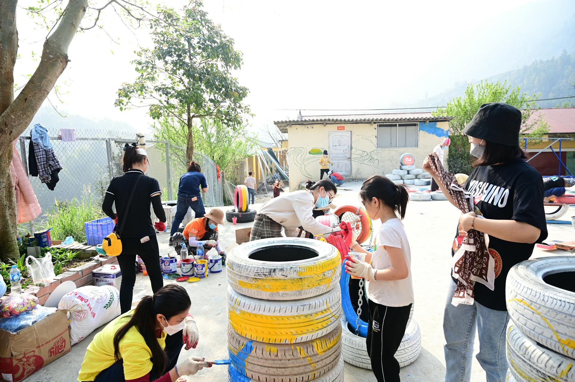 Children and adults collaborate on a colorful tire painting project in an outdoor community space.