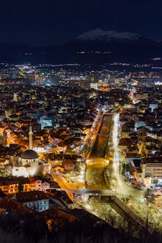 Captivating aerial shot of Prizren at night showcasing illuminated cityscape and distant mountains.