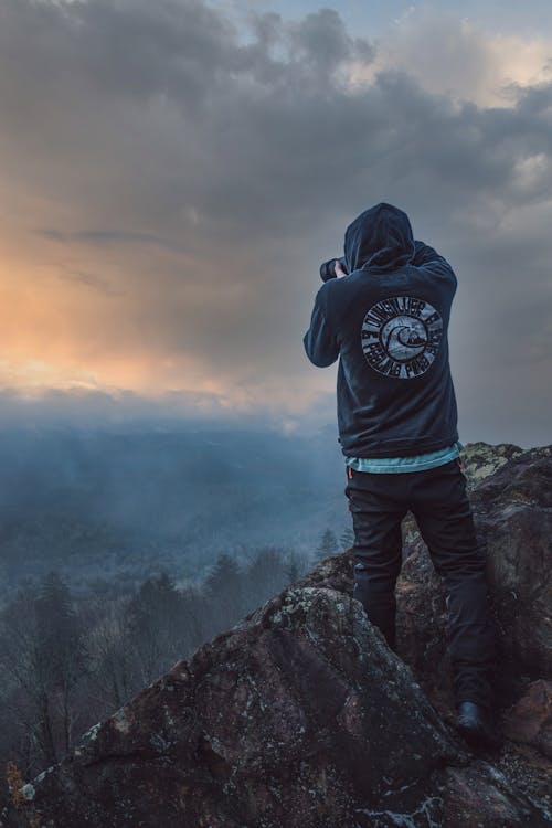 Backview of Man in Black Hoodie Standing on a Cliff of Rock Formation