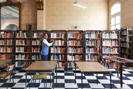 A librarian organizing books in a spacious, classic library with checkered flooring.