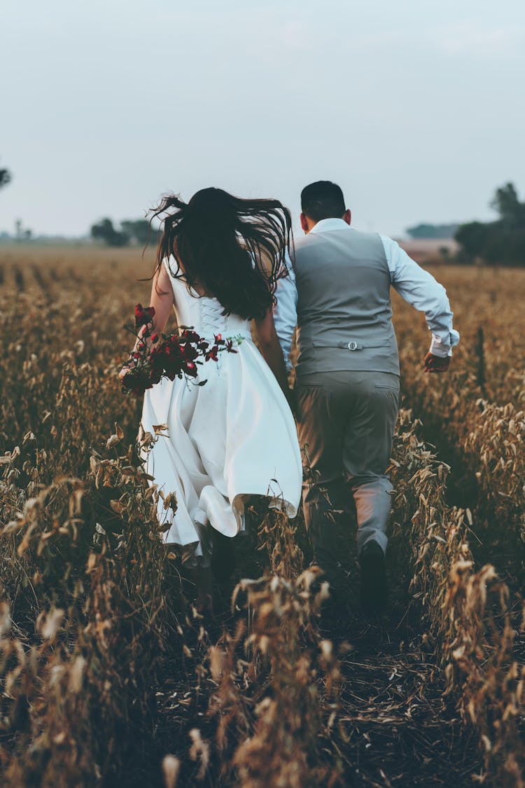 Bride And Groom Running Through Field