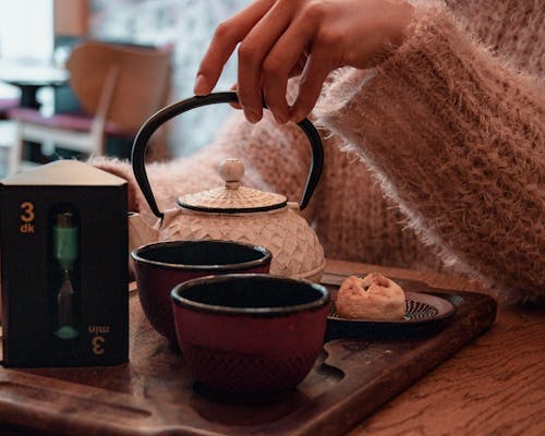 Person Holding Black and White Ceramic Teapot