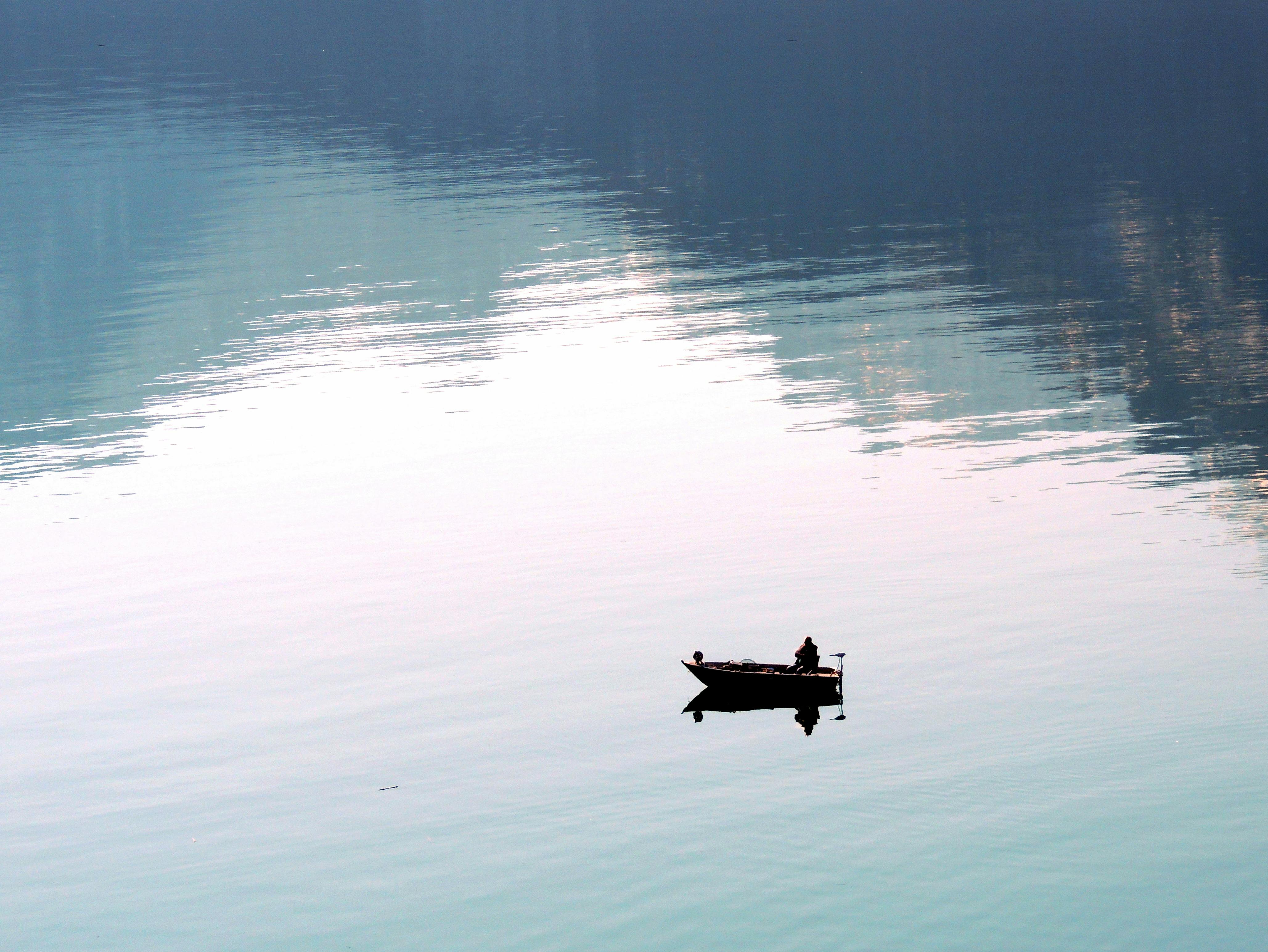 A lone fisherman in a small boat on the peaceful waters of Lake Wolfgang, Austria.