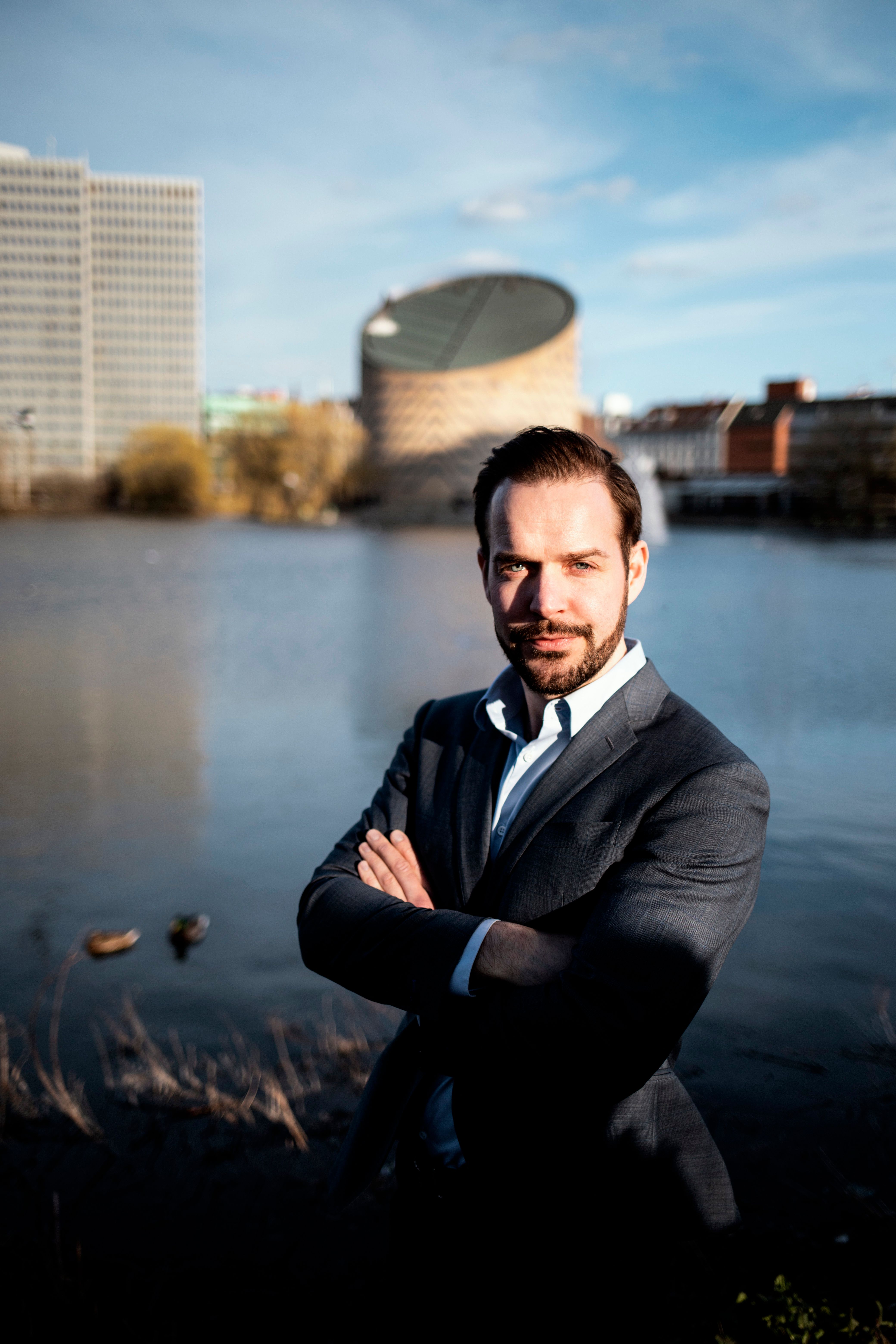 Portrait of a well-dressed man posing confidently by the Copenhagen waterfront with an urban backdrop.