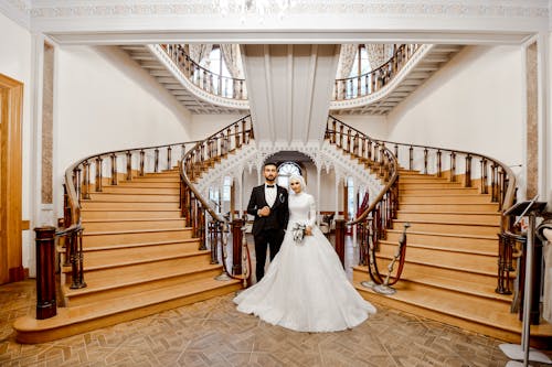 Man and Woman in Wedding Dress Standing on Brown Wooden Staircase