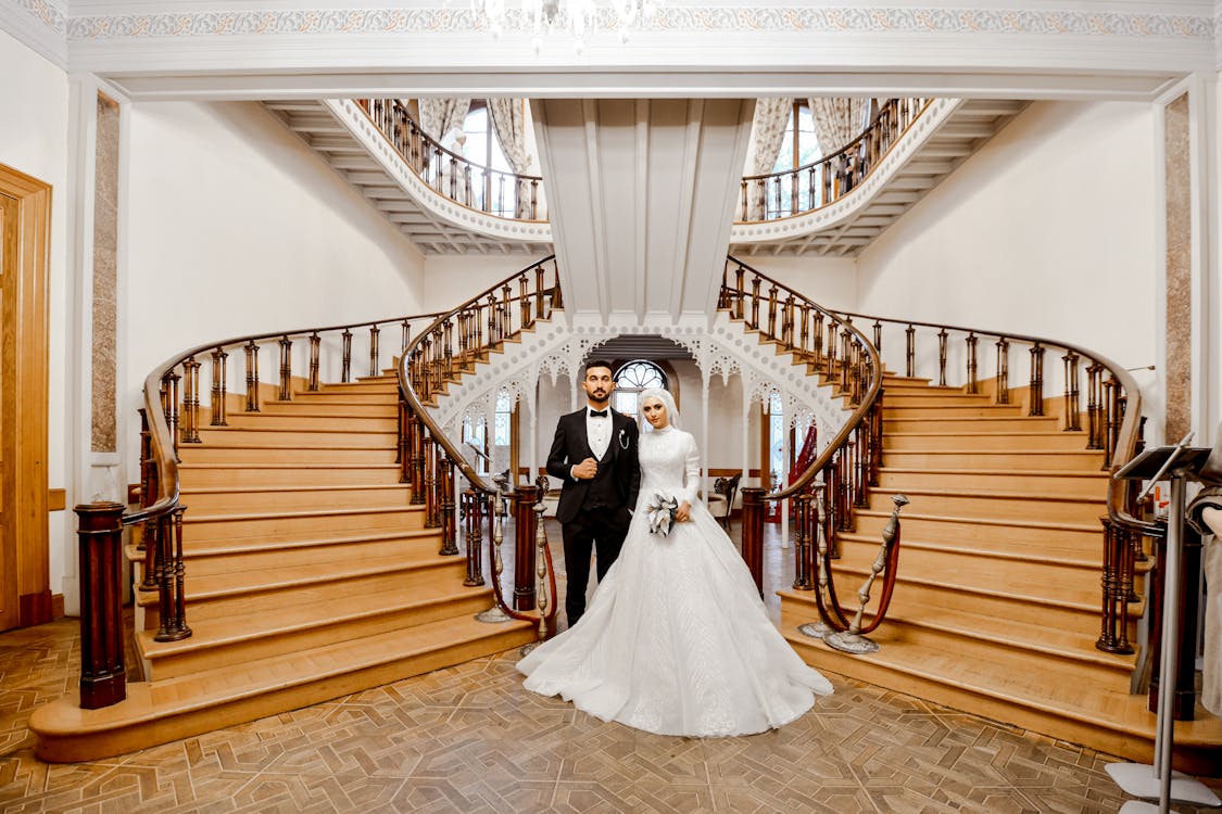 Man and Woman in Wedding Dress Standing on Brown Wooden Staircase