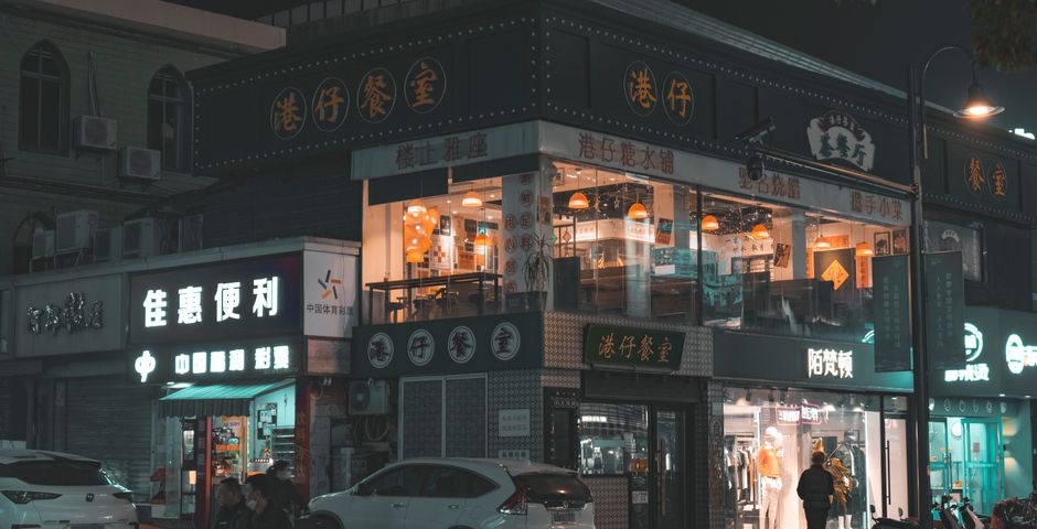 Illuminated shopfronts along a busy street at night — the F&B podium is where the population is generated