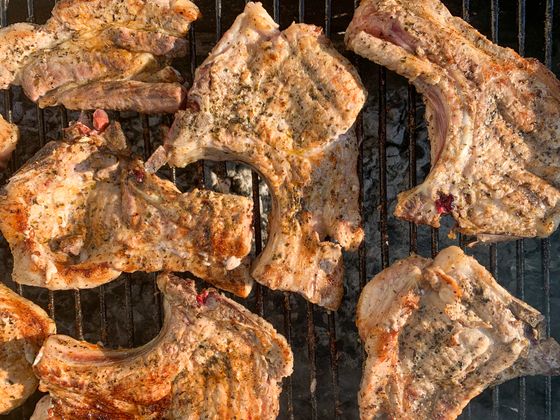 Bone-in pork chops rubbed with dried herbs searing on a charcoal grill grate