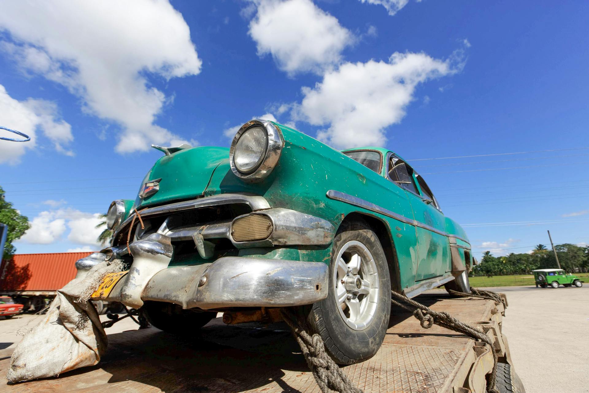 A vintage classic car with a damaged bumper under a blue sky, showcasing nostalgia.