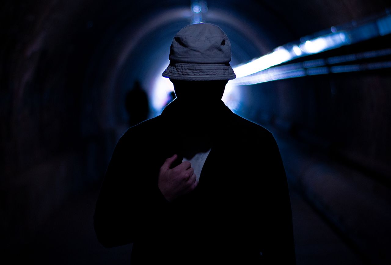 silhouette of a mysterious man wearing a hat in a dimly lit urban tunn