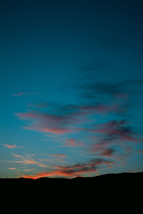 Free Stunning sunset with vibrant colors and wispy clouds over silhouetted hills. Stock Photo