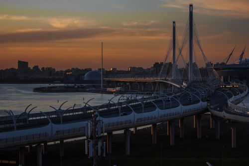 Free Dramatic urban cityscape featuring a striking modern bridge spanning a calm river at sunset. Stock Photo