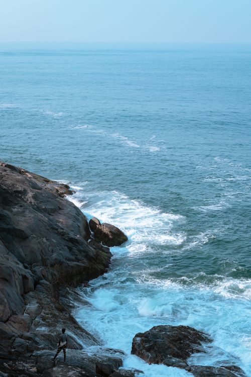 Free A scenic view of a rocky coastline with clear blue sea and gentle waves crashing. Stock Photo