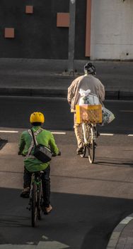 Two cyclists riding bicycles on a sunlit street in Dubai, helmets on, focused on city commute.