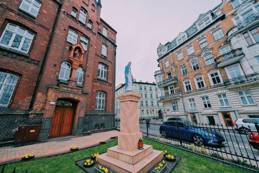 Street view of Virgin Mary statue against historic redbrick facades in Poznań, Poland.