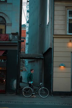 A man walks with his bicycle down a narrow modern street in downtown Copenhagen.